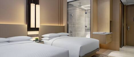 Una habitación de hotel moderna con dos camas, cabina de ducha de vidrio y una mesita de noche con una planta.