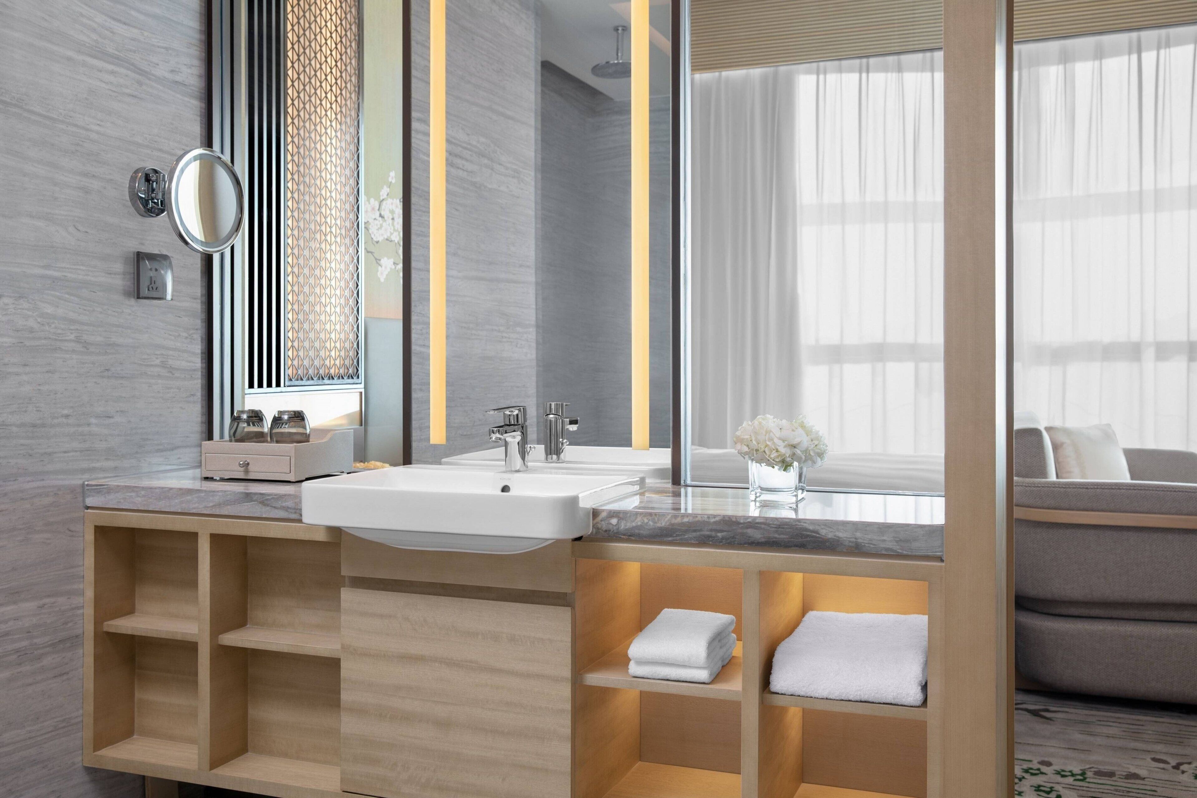 A modern bathroom with a large mirror, two sinks, and built-in shelves for towels.