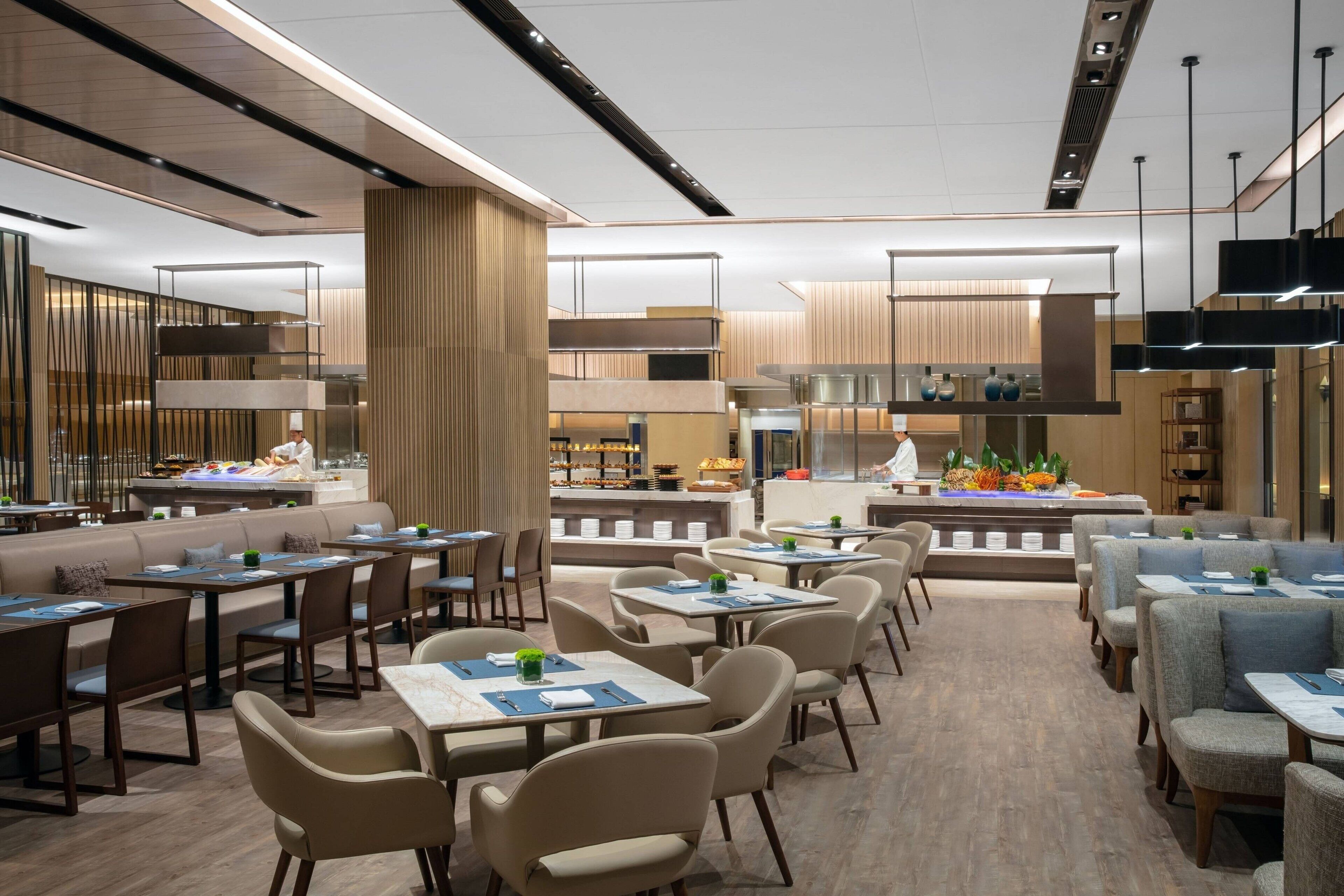 A modern restaurant with a central bar area, multiple seating options including booths and tables, and a visible kitchen in the background.