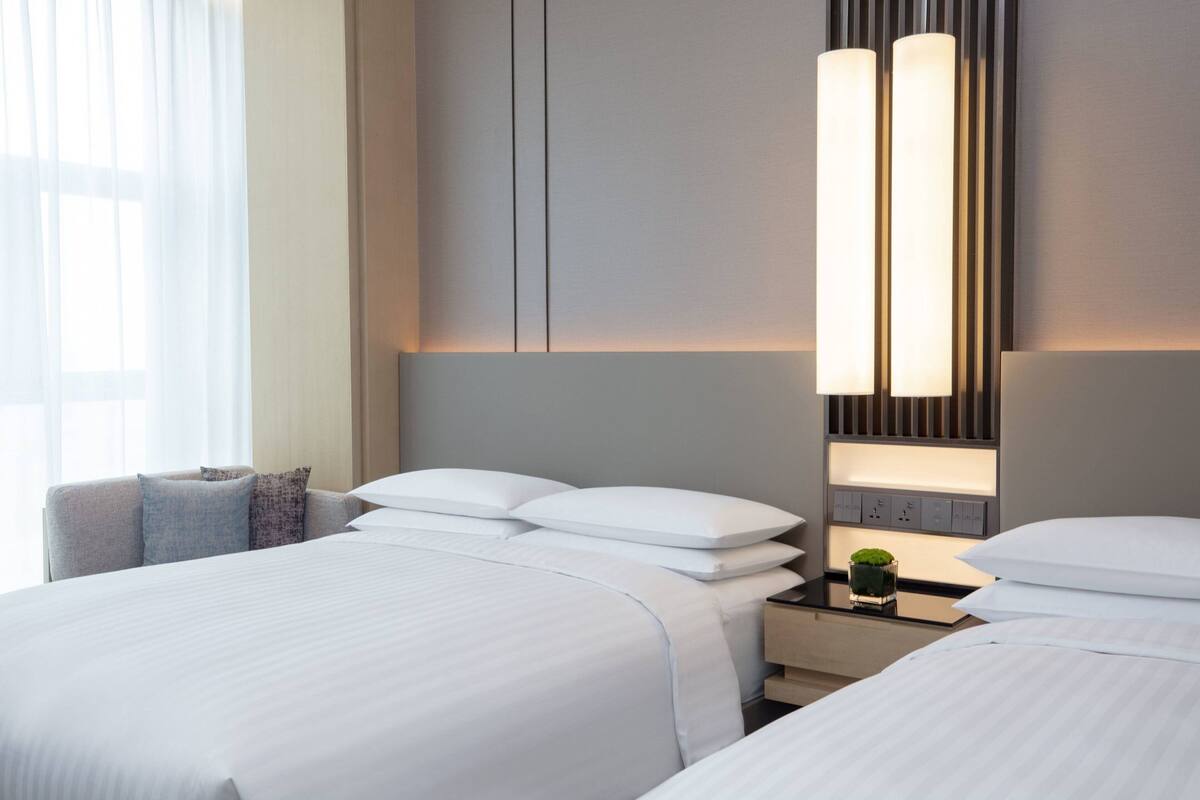 A hotel room with two beds, a nightstand, and a wall-mounted light fixture.