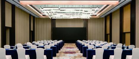 Une salle de conférence avec des rangées de tables et de chaises, une moquette à motifs et un design de plafond moderne.