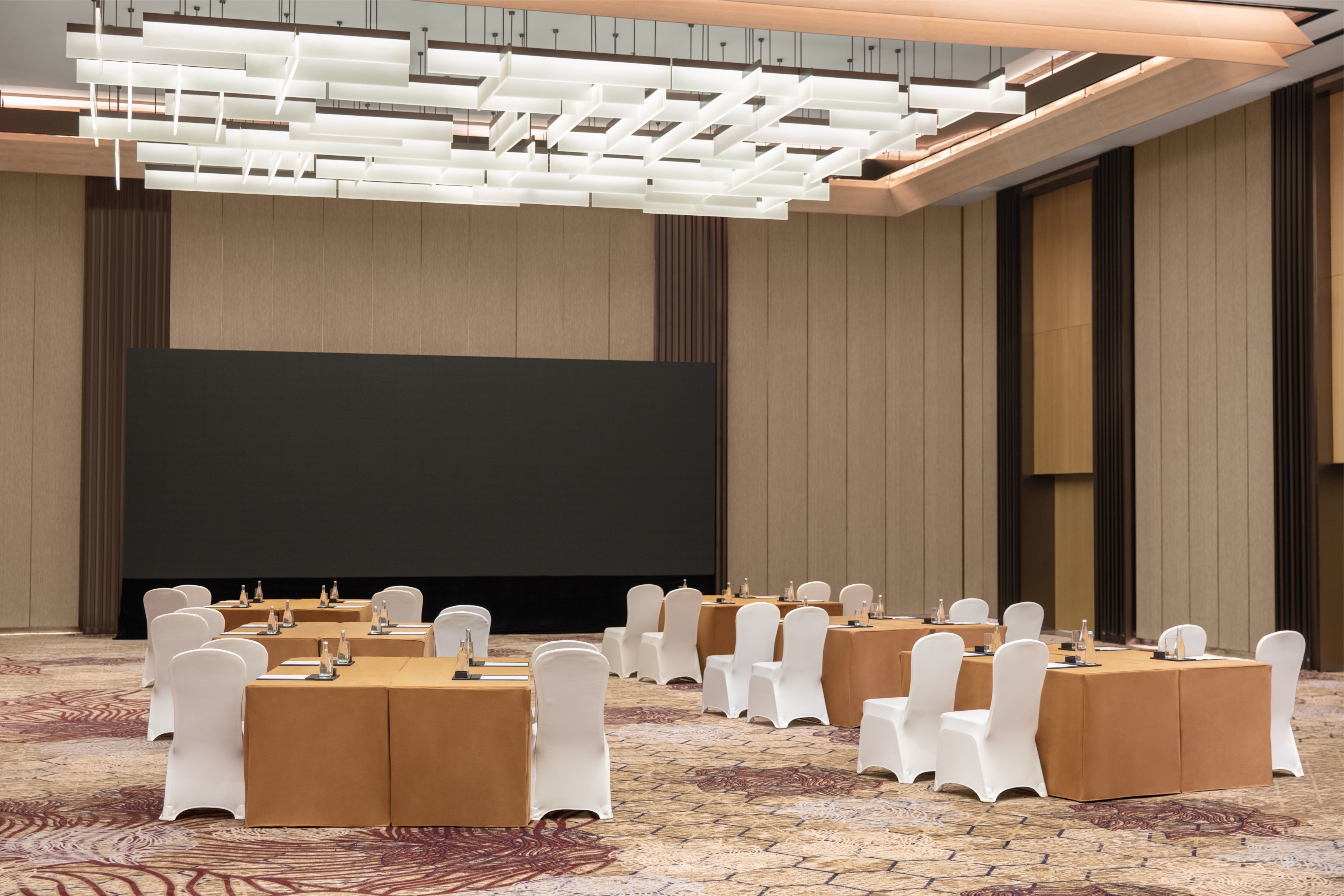 A conference room with multiple tables, chairs, and a large screen.