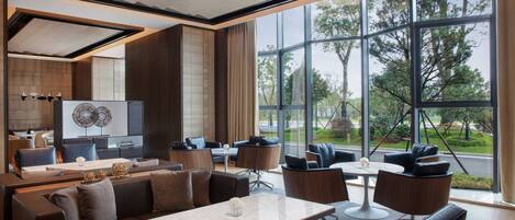 A modern hotel lobby with a large seating area, a reception desk, and large windows offering a view of the outdoors.