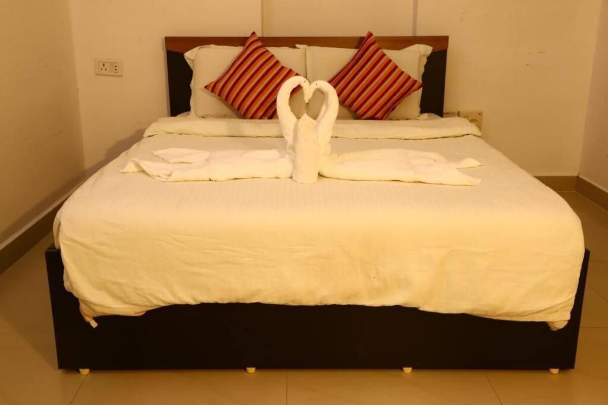 Un lit bien fait, avec une couette blanche, deux oreillers et une serviette pliée en forme de cœur posée sur le lit.