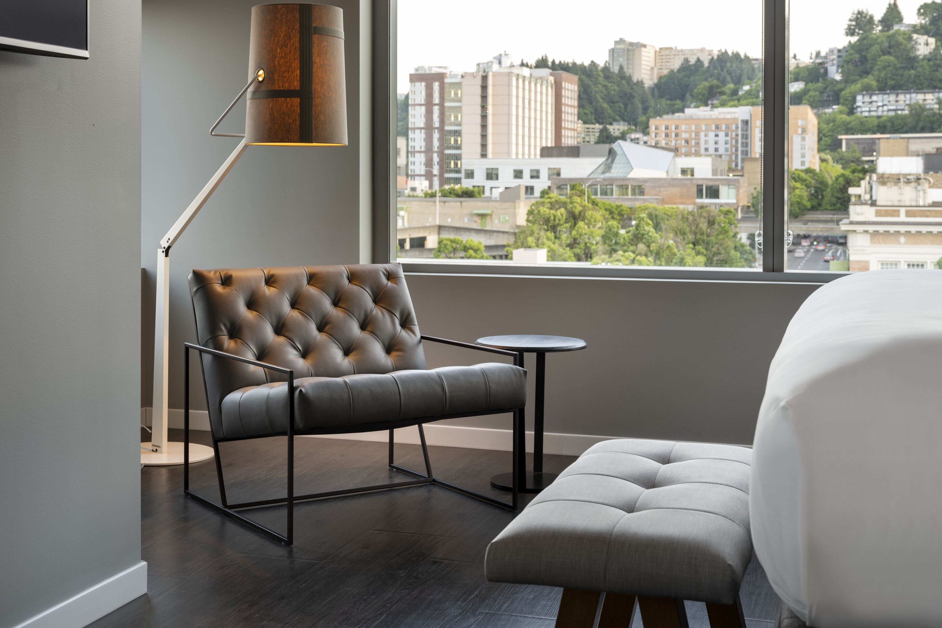 A modern hotel room with a tufted leather armchair, a round side table, and a large bed.