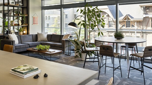 Un salon moderne avec un canapé, une table basse et des fauteuils, de grandes fenêtres et des plantes d’intérieur.