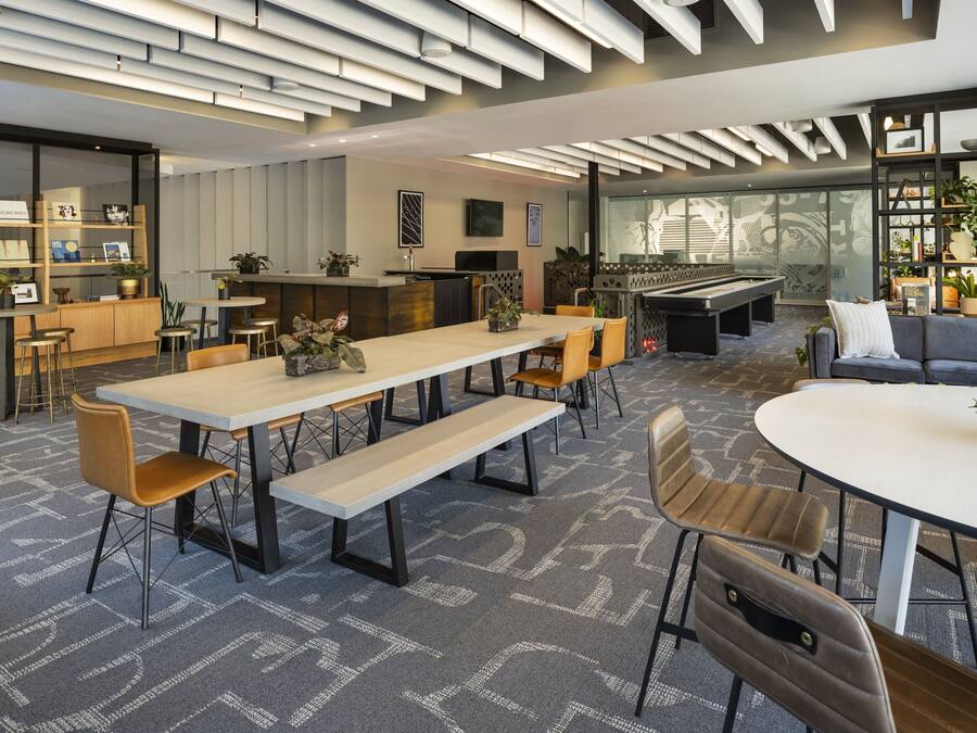 A modern lounge area with a long table, multiple chairs, a sofa, and a bar area.