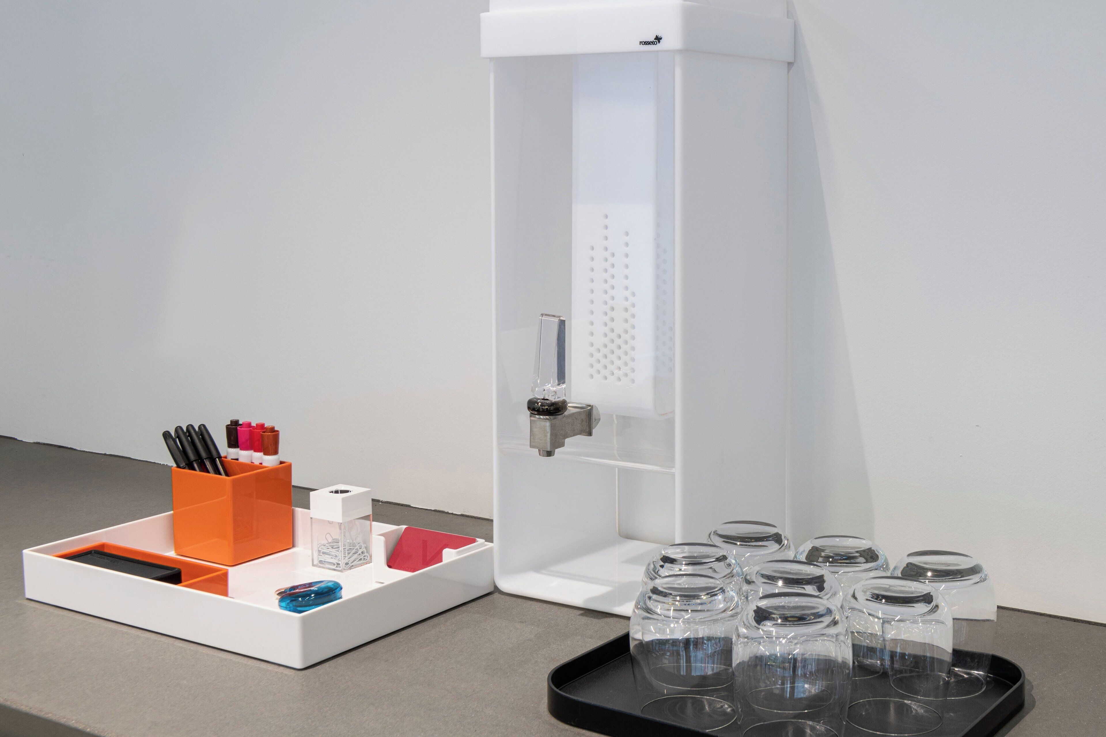 A white cabinet with a handle, a tray with pens and a red napkin, and several clear glass jars on a black tray.