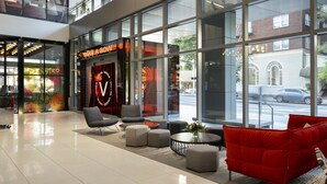 Un hall d’entrée moderne avec de grandes fenêtres, un canapé rouge et un espace salon agrémenté de poufs et d’une table.