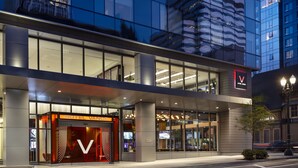 Un hôtel moderne, reconnaissable à son logo en forme de « V » bien visible, à ses grandes fenêtres en verre et à son entrée bien éclairée.