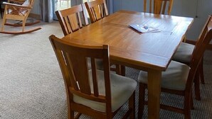 Zona pranzo con tavolo e sedie in legno, lampadario e vista attraverso una finestra.