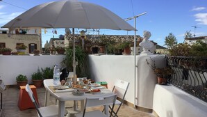 A rooftop terrace with a table set for breakfast, surrounded by potted plants and a white umbrella. - Agliastrello Rooms (Noto)