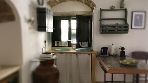 A kitchen with a stone archway, a sink, a stove, and a dining table with chairs. - Agliastrello Rooms (Noto)