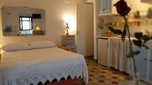 A bedroom with a bed, a dresser, a mirror, a desk, and a small refrigerator. - Agliastrello Rooms (Noto)