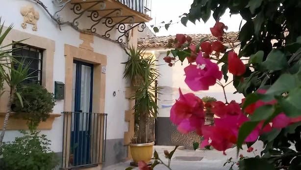 A courtyard with a building featuring a blue door and a balcony with decorative ironwork. - Agliastrello Rooms (Noto)