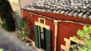 A red building with a tiled roof, a green door, and a potted plant. - Agliastrello Rooms (Noto)