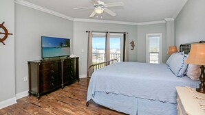 A bedroom with a bed, a dresser, a ceiling fan, a TV, and a view of the outdoors. - Gulf View Condo~ Paradise Shores 403 Sunset Paradise (Mexico Beach)