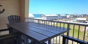 A balcony with a wooden table and chairs, overlooking a coastal area with buildings and a clear sky. - Gulf View Condo~ Paradise Shores 403 Sunset Paradise (Mexico Beach)