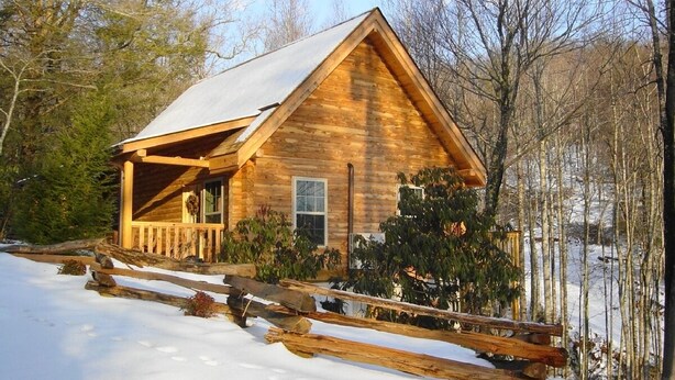 A log cabin with a snow-covered roof, surrounded by trees and a wooden fence. - New red cedar log home just off the blue ridge parkway in Little Switzerland, NC (spruce pine)