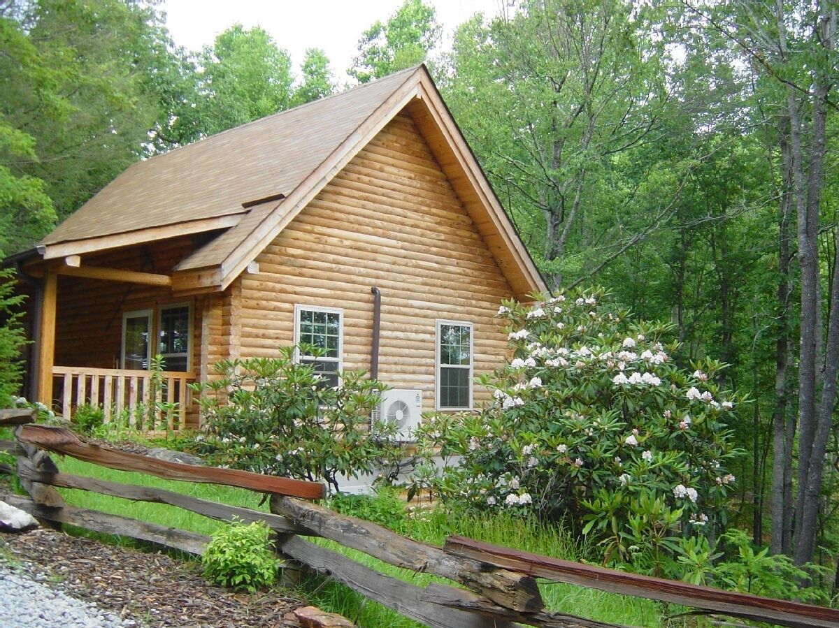 A log cabin with a porch, two windows, and a small garden with white flowers.