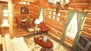 A cozy log cabin interior with a dining area, a sofa, a TV, and a chandelier. - New red cedar log home just off the blue ridge parkway in Little Switzerland, NC (spruce pine)