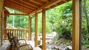 A wooden deck with rocking chairs, surrounded by lush greenery and a stone pathway. - New red cedar log home just off the blue ridge parkway in Little Switzerland, NC (spruce pine)