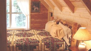 A cozy bedroom with a wooden ceiling, a quilted bedspread, a bedside lamp, and a window with curtains. - New red cedar log home just off the blue ridge parkway in Little Switzerland, NC (spruce pine)