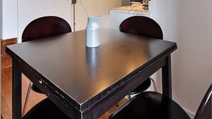 Ein Essbereich mit einem dunklen Holztisch, zwei Stühlen, einem weißen Wasserkocher und einer unter der Decke angebrachten Klimaanlage.