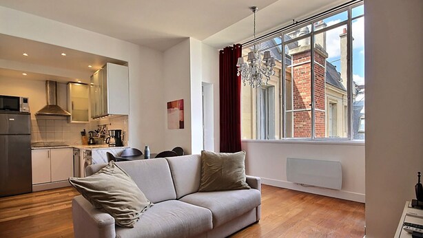 Ein modernes Wohnzimmer mit Sofa, Esstisch und einer Küche im Hintergrund.