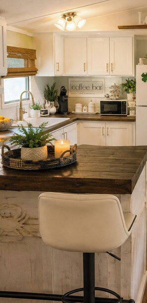 A kitchen with white cabinets, a coffee bar sign, a microwave, and a bar stool.