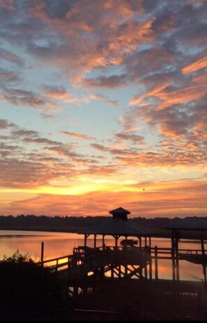 Une vue sur le coucher de soleil, avec une jetée en bois et un kiosque au bord d’un lac paisible.
