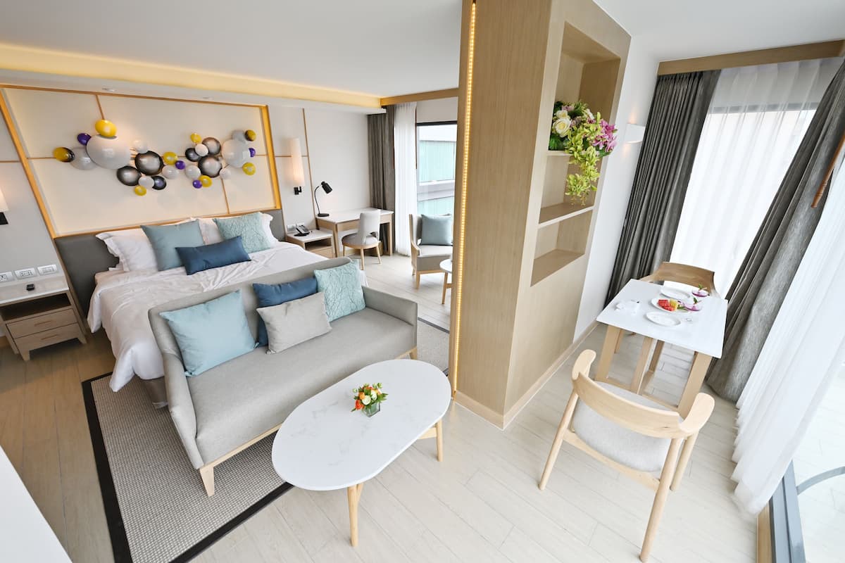 A modern hotel room with a bed, sofa, dining table, and chairs.