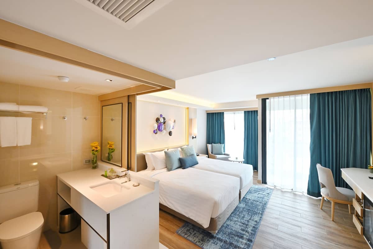 A modern hotel room with a large bed, a desk, a bathroom, and a view of the outdoors.