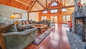 A spacious living room with a high wooden ceiling, a stone fireplace, and a large window allowing natural light. - Luxurious Woodstock Home Rental Catskill Mountains Views & Private Retreat (Bearsville)