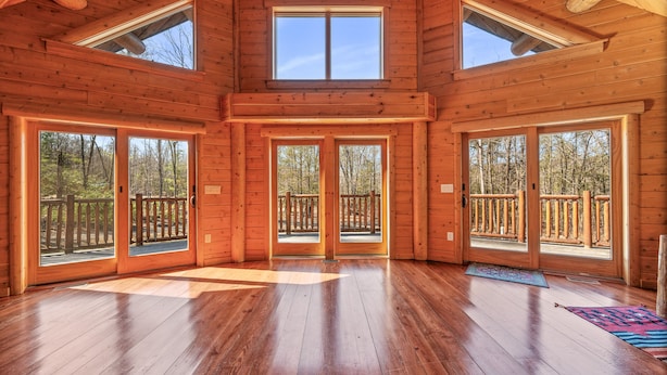 A spacious wooden cabin with large sliding glass doors leading to a deck, multiple windows, and a high ceiling with skylights. - Luxurious Woodstock Home Rental Catskill Mountains Views & Private Retreat (Bearsville)
