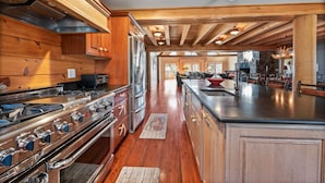A spacious kitchen with wooden cabinets, a large island, and a stone accent wall. - Luxurious Woodstock Home Rental Catskill Mountains Views & Private Retreat (Bearsville)