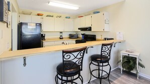 A kitchen with a refrigerator, microwave, toaster, and bar stools. - Lots of Space, Beachview, Easy ~ Coastal Sunshine (Cape San Blas)