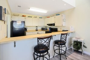 A kitchen with a refrigerator, microwave, toaster, and bar stools.