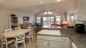 A spacious kitchen with a dining area, a living room with a sofa and TV, and a large window with a view. - Beachfront, Spacious, Community Pool, Pet Friendly! 2-The-Beach (Indian Pass)