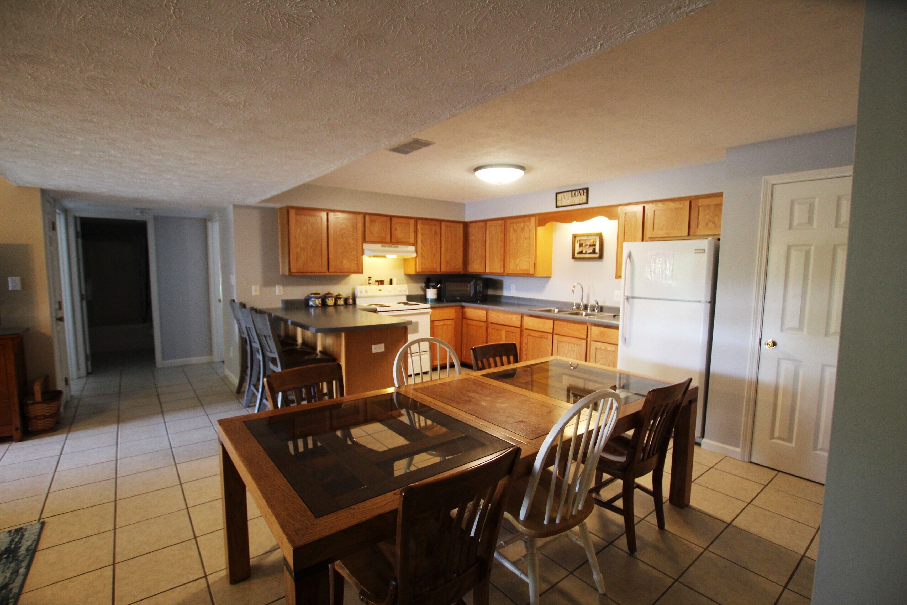 A kitchen with wooden cabinets, a dining table, chairs, a refrigerator, and a microwave.