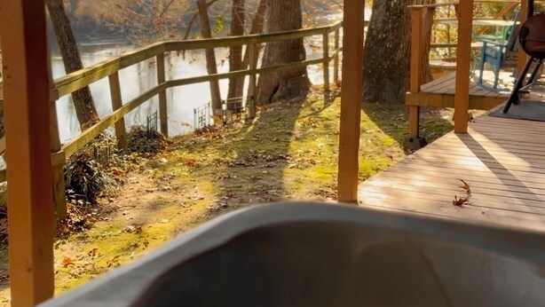 Un jacuzzi con terraza de madera y vista a un lago y árboles.