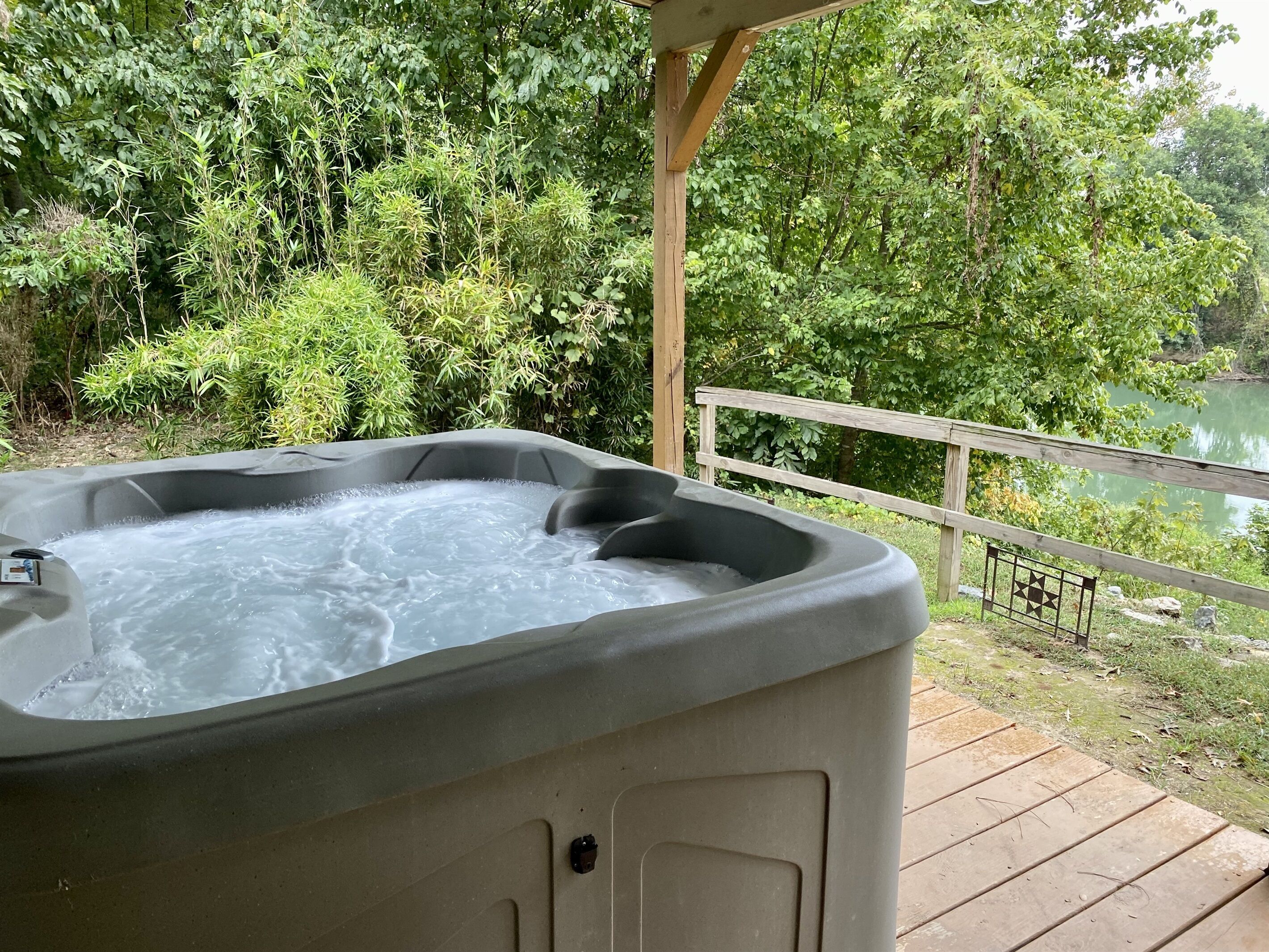 Ein Whirlpool auf einer Holzterrasse mit Blick auf einen See und dichtes Grün.