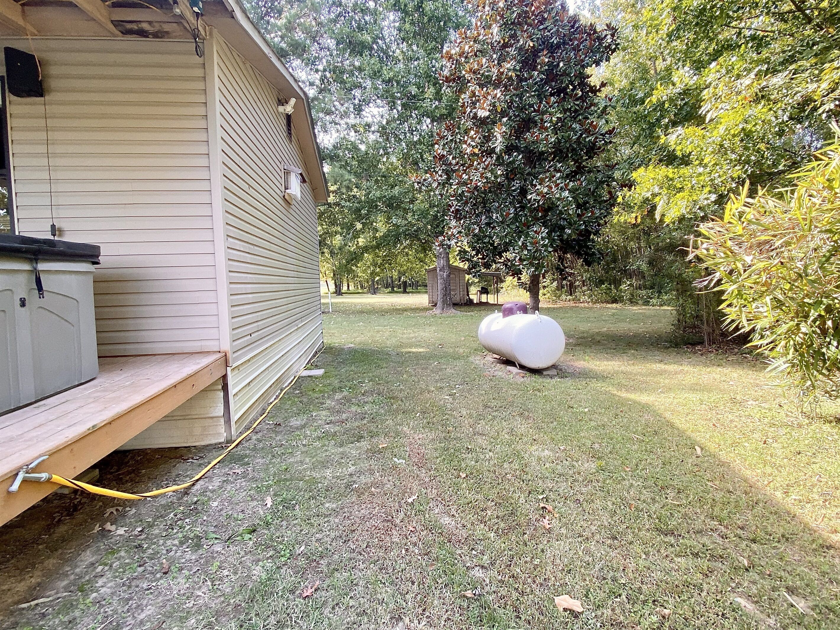 A wooden building with a covered porch, a large white water tank, and a grassy yard with trees.