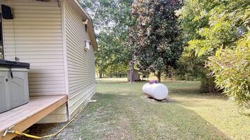 A wooden building with a covered porch, a large white water tank, and a grassy yard with trees.