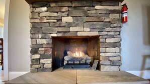 A stone fireplace with a fire burning inside, a fire extinguisher mounted on the wall, and a wooden floor. - Hot tub, Campfire ring and great location! (Harpers Ferry)