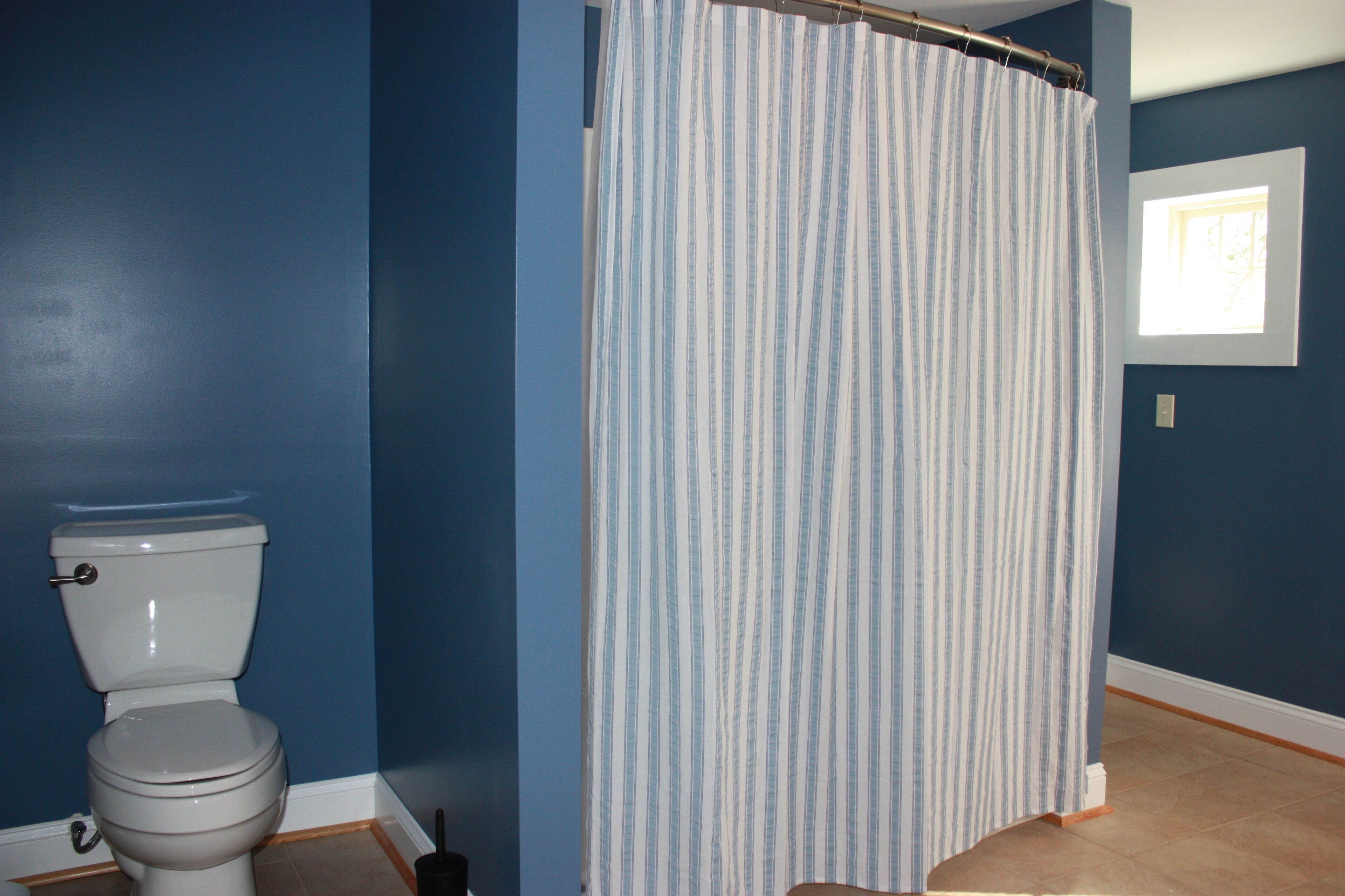 A bathroom with a toilet, a shower curtain, and a window.