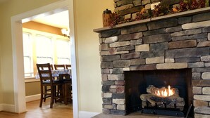 A stone fireplace with a fire, wooden dining table, and chairs in a room with wooden flooring. - Hot tub, Campfire ring and great location! (Harpers Ferry)