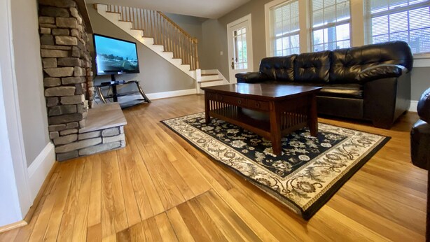 A living room with a stone fireplace, a wooden coffee table, a black leather sofa, and a staircase leading to another level. - Hot tub, Campfire ring and great location! (Harpers Ferry)