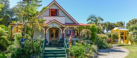 A two-story building with a red roof and white walls, surrounded by lush greenery and a small garden.