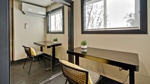 Una habitación moderna con una mesa de vidrio, dos sillas, una planta en maceta y un amplio ventanal con vistas a árboles.